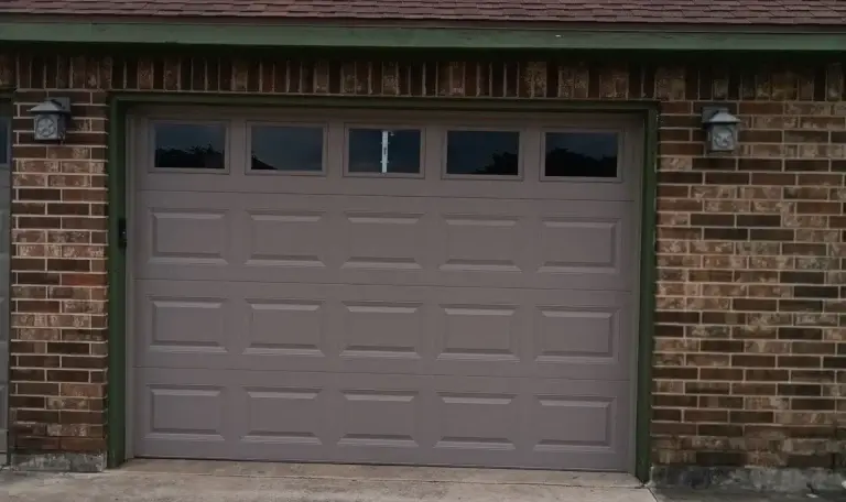 Almond raised-panel garage door with a window row on a red brick home