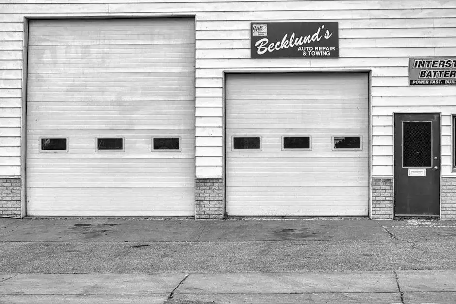 Two white sectional overhead doors on a lap-sided auto shop, with a Becklund's Auto Repair and Towing sign between them