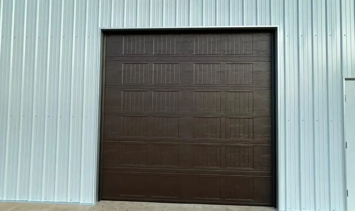 Dark brown wood-grain sectional garage door on a white metal shop building