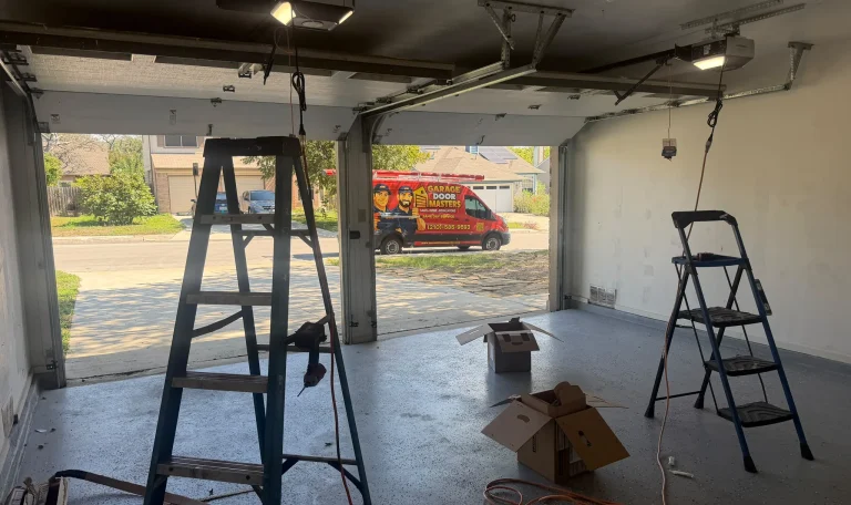 Garage work area with open doors, ladders, equipment boxes, electrical cords, and a service vehicle outside.