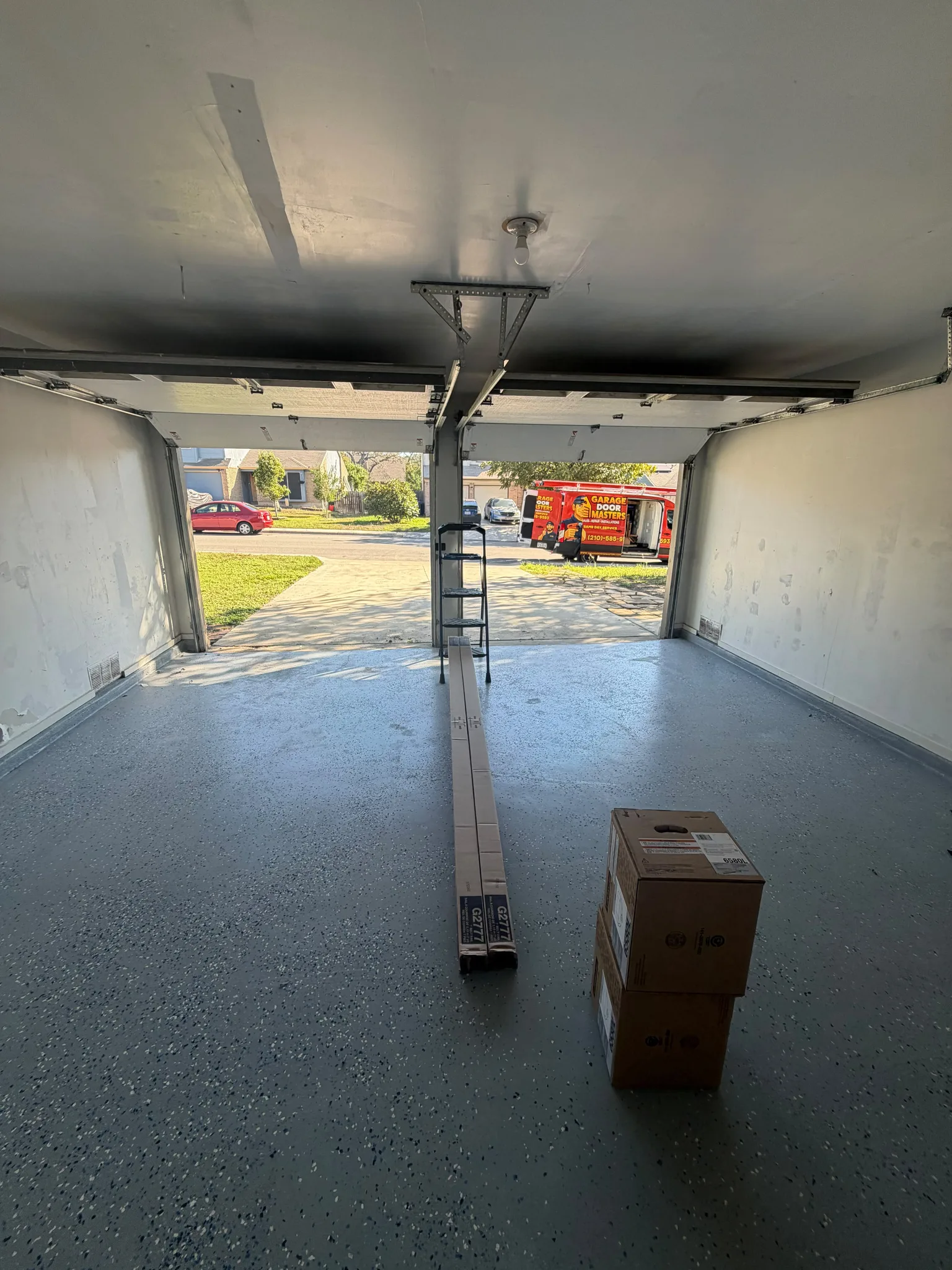 Interior view of an empty garage looking through the open doorway toward the driveway and residential street.