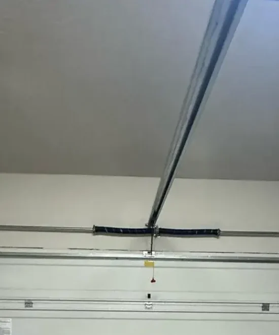 Inside a garage looking at the top of a closed white door, spring shaft and opener rail overhead