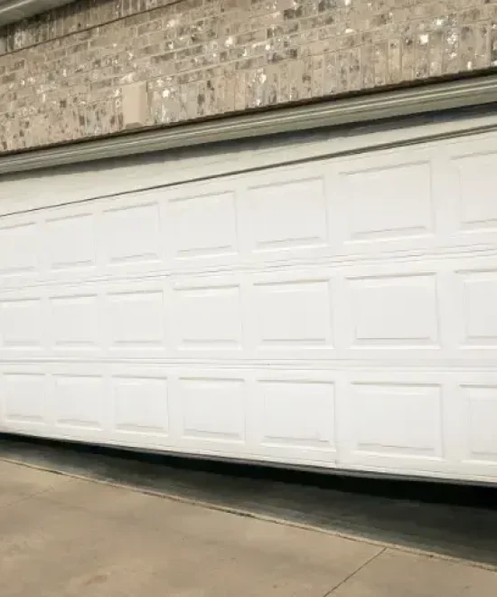 White sectional garage door hanging crooked in its opening with a gap along the bottom edge