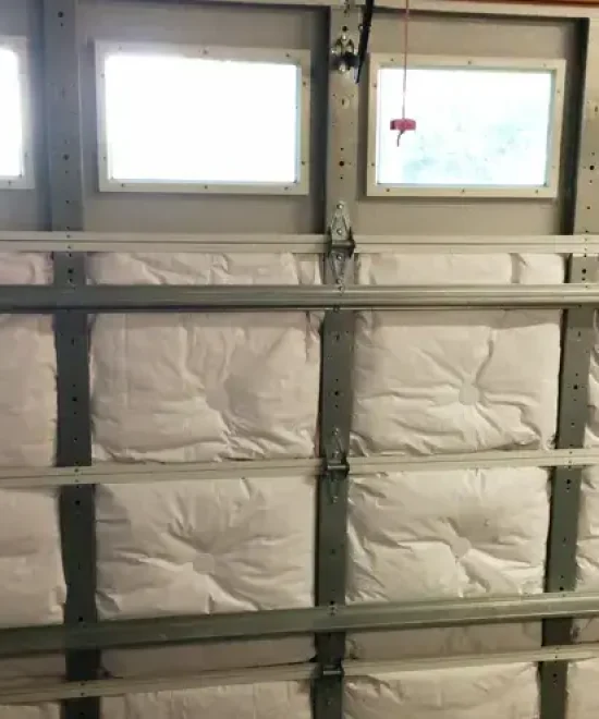 White insulation batts fitted into the panels of a closed garage door with a row of windows