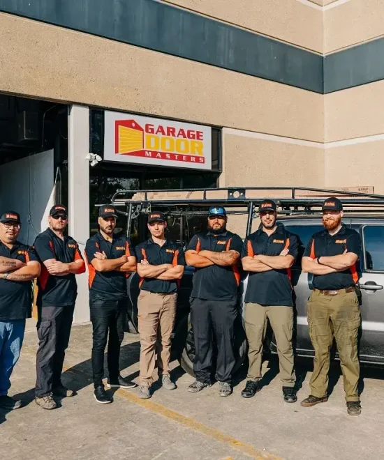 Seven Garage Door Masters technicians with arms crossed outside the shop, beside a branded pickup truck
