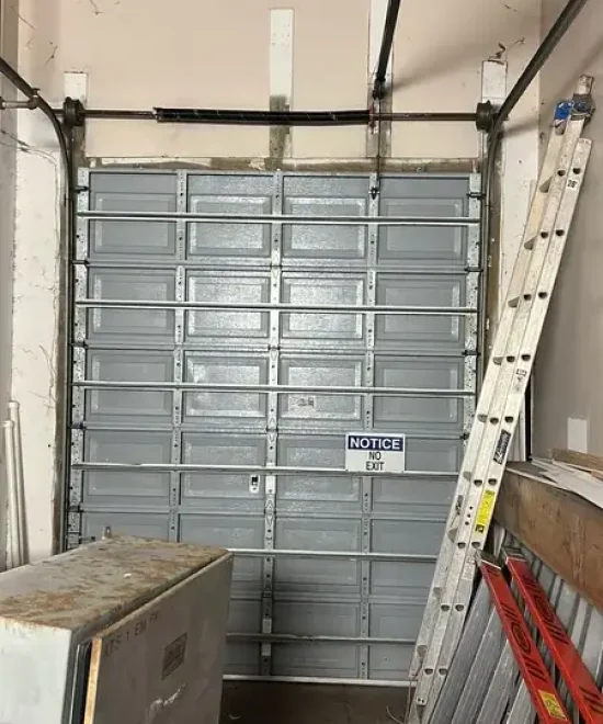 Gray sectional garage door inside an industrial space, No Exit notice sign and ladders leaning nearby