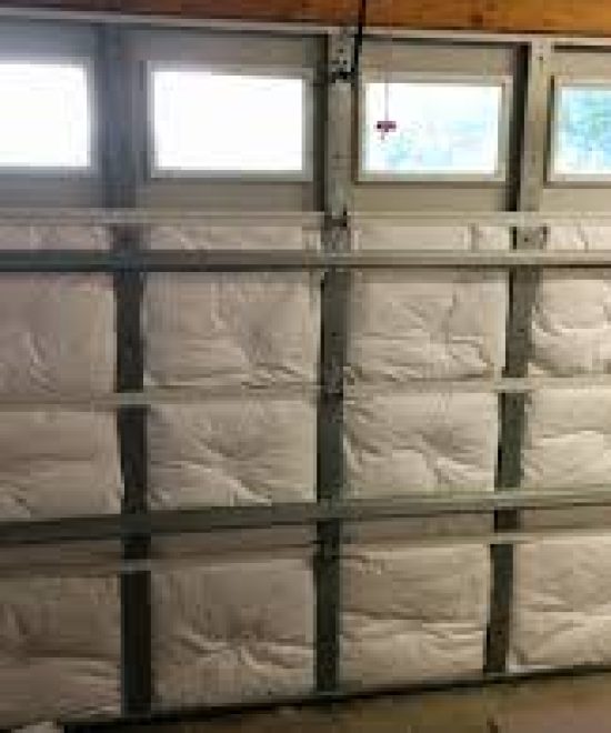 White insulation batts fitted into the panels of a garage door with a row of windows