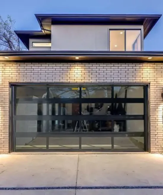 Full-view glass and aluminum garage door lit at dusk on a modern white brick home