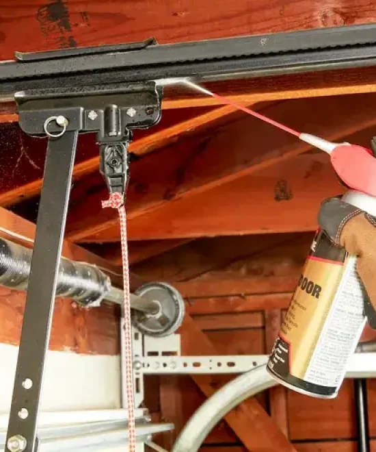 Gloved hand spraying lubricant onto a garage door opener rail and trolley