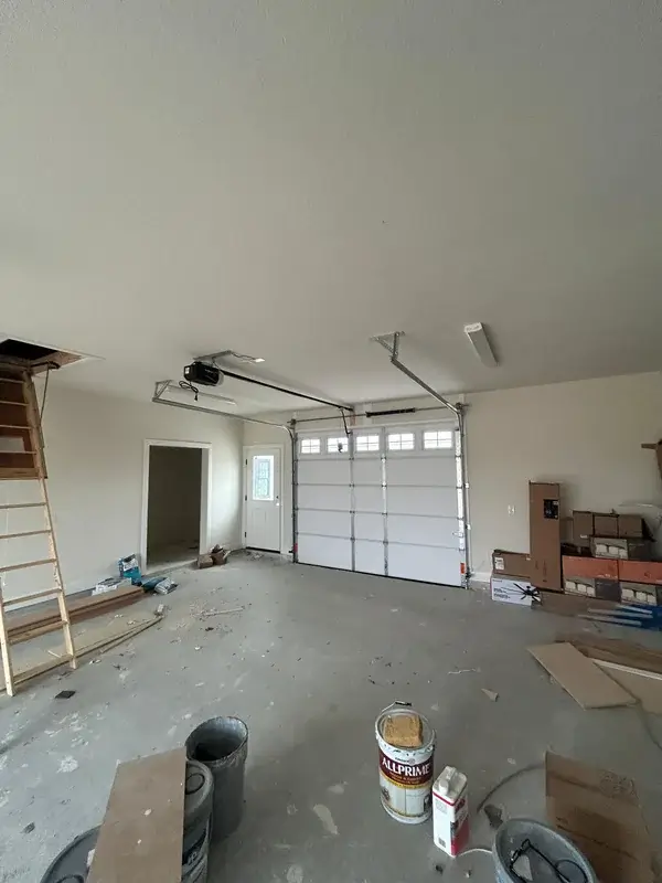 Ceiling-mounted opener and rail above a white sectional garage door in an unfinished garage