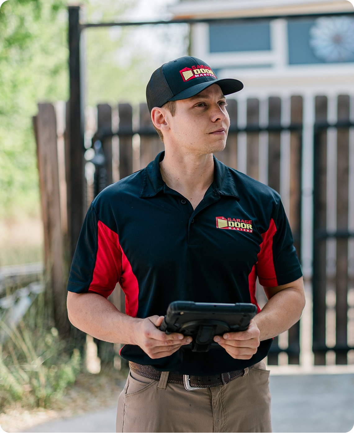 Technician in a black and red Garage Door Masters polo holding a rugged tablet outdoors