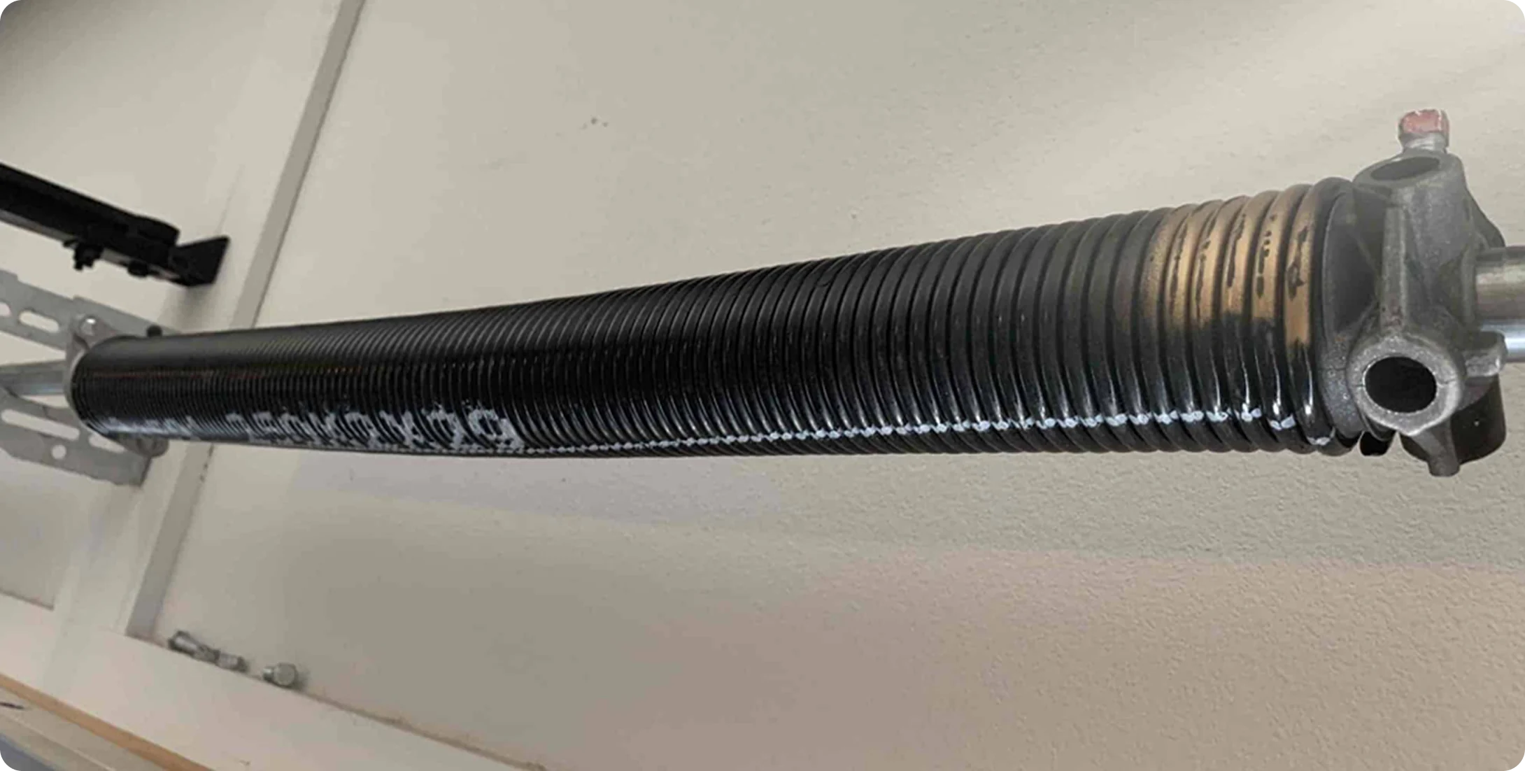Close-up of a black garage door torsion spring and winding cone mounted on the wall