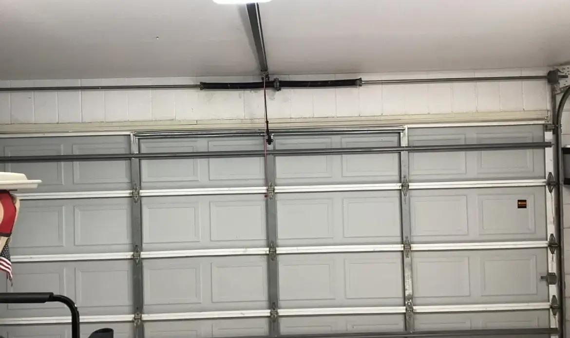 Closed gray sectional garage door seen from inside a garage with opener rail and torsion spring above