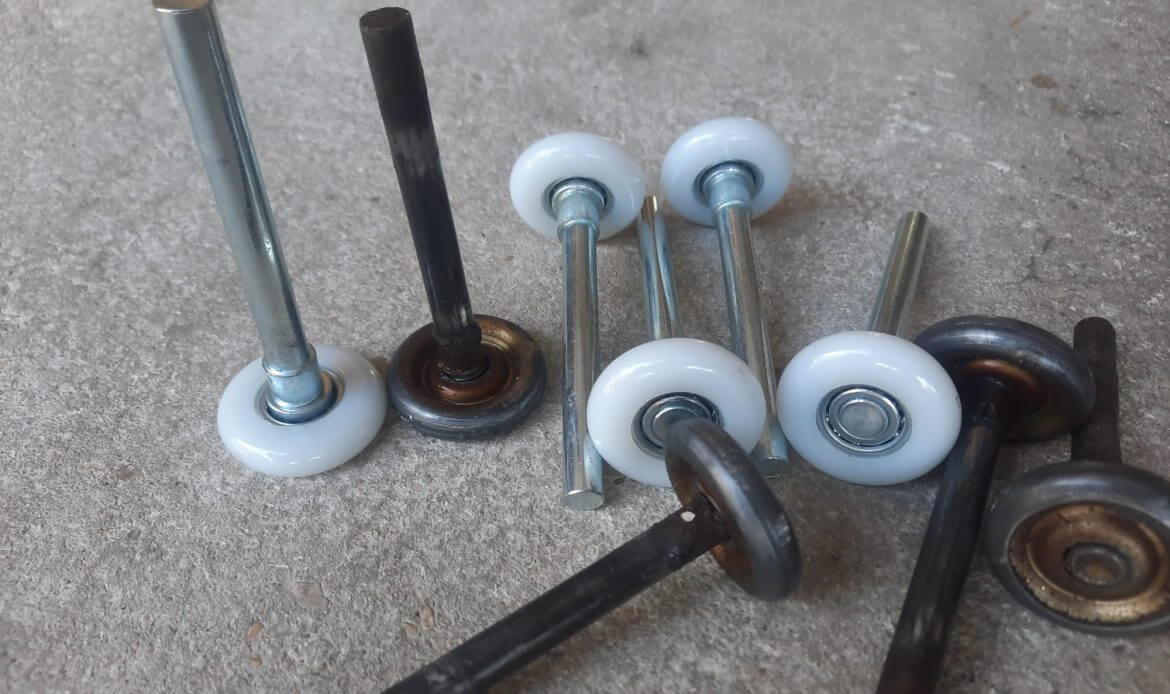New white nylon garage door rollers next to worn rusted steel rollers on concrete