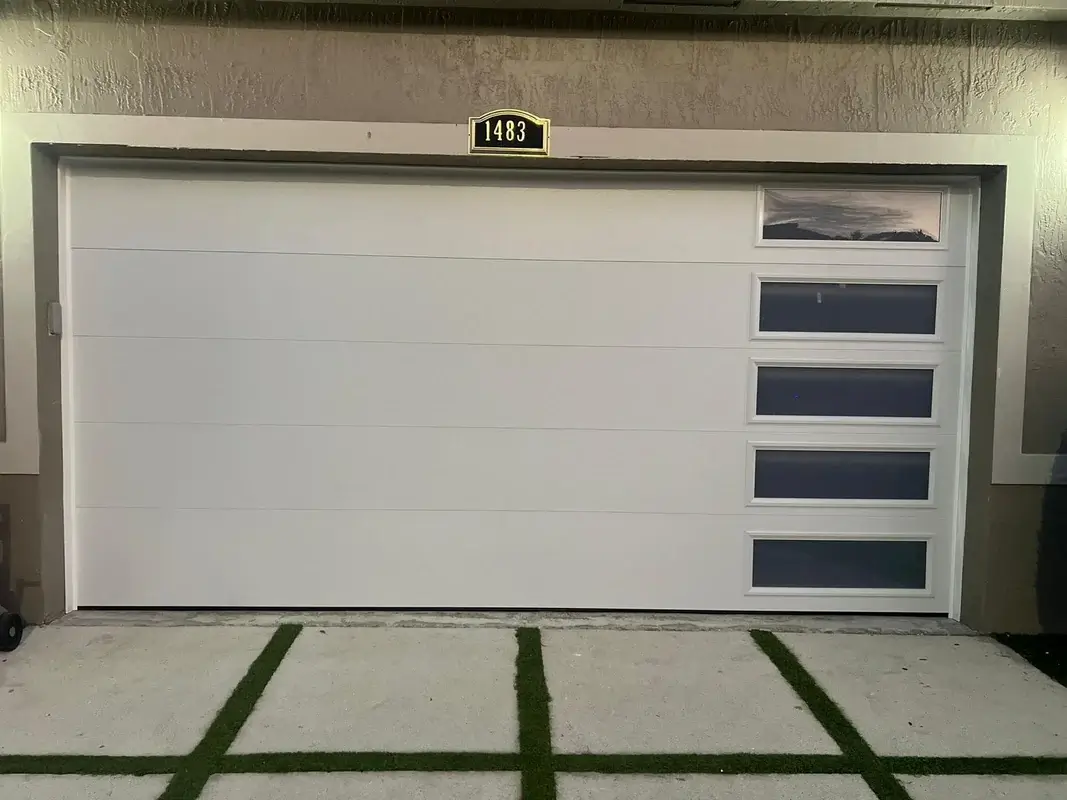 White long-panel double garage door lit at night, with a vertical row of windows and a 1483 address plaque